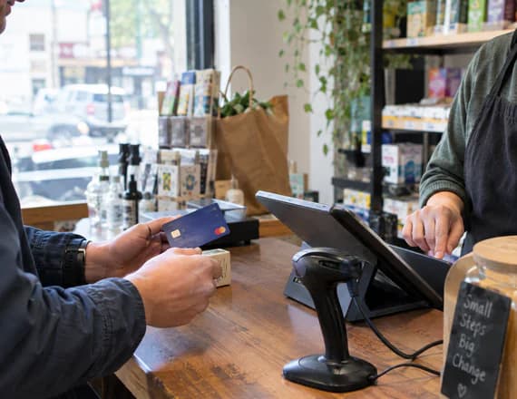 A customer paying by card at a shop counter, a barcode scanner beside the till